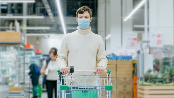 A Man in a Medical Mask Stands in a Supermarket with a Food Cart Timelaps alt