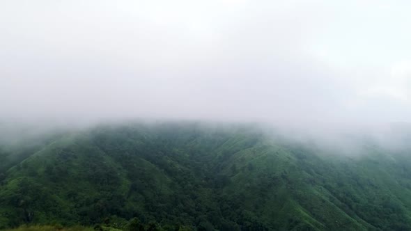 Dense fog covering top of mountain with lush forest after last rains of autumn season in India alt