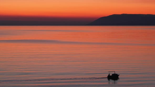 Small Boat Silhouette On Calm Sea At Sunset