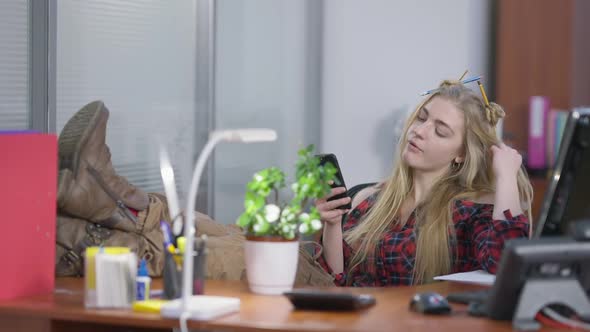Relaxed Carefree Hipster with Feet on Table Surfing Internet on Smartphone Chewing Gum alt