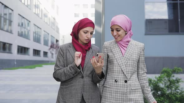 Two Young Muslim Women Wearing Hijab Headscarf Look at Phone and Shows Something