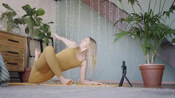 Young Woman Does Yoga Talking Via Videocall Using Phone alt
