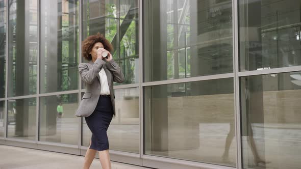 Afro American businesswoman in city using smart phone with takeaway coffee