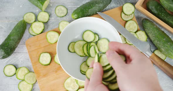 Men Hands Put Pieces of Sliced Cucumber in Bowl.  alt