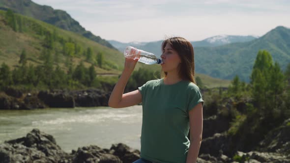 Pretty Woman Refreshes Drinking Water on Rocky Riverbank alt