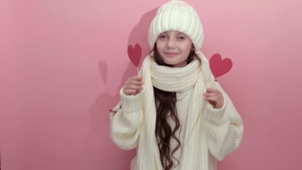 Happy Young Girl Wearing White Knitted Sweater Holding Red Hearts Over Eyes alt