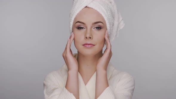 Woman Smoothes Her Face in Bath Towel and Robe Isolated on Grey alt