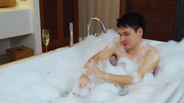 young man washing body with foam in bathtub