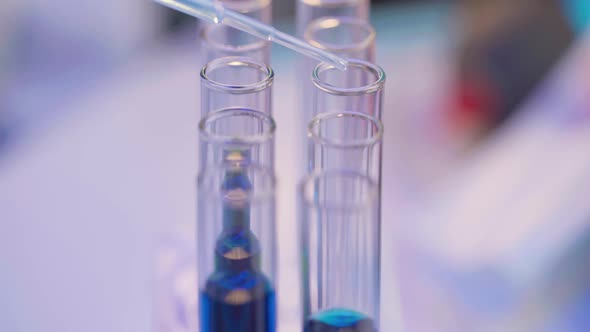 Close Up of Pipette Dropping Samples of Color Liquid Into Test Tubes in Laboratory alt