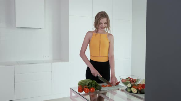 Young Woman Slicing Red Pepper For Vegetable Salad. White Modern Kitchen.