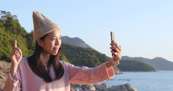 Woman taking video call on cellphone over seascape alt