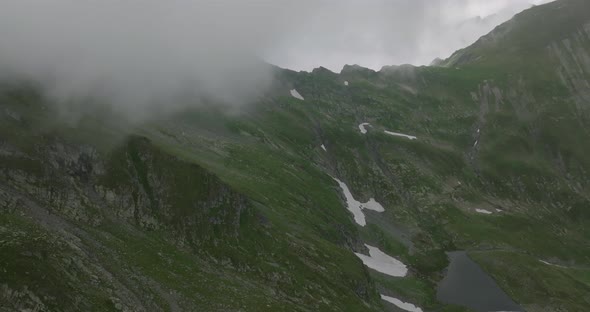 aerial footage of mountain lake and mountain range with snow and peaks in clouds alt