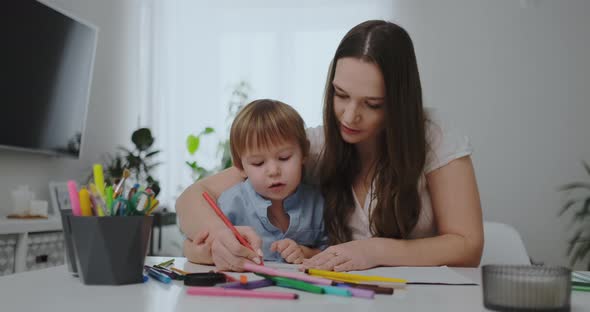 A Family of Two Children and a Young Mother Sitting at the Table Draws on Paper with Colored Pencils alt
