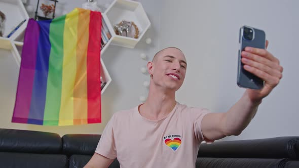 Queer Nonbinary Bald Influencer Waves to His Followers on Social Media with Rainbow Pride Flag in alt
