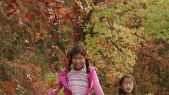 Two young girls in Fall throwing pile of leaves