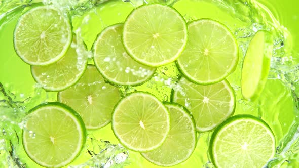 Super Slow Motion Shot of Lime Slices Falling Into Water on Green Background at 1000Fps. alt