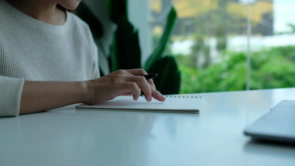 Closeup of a woman reading and writing on a blank notebook on the table