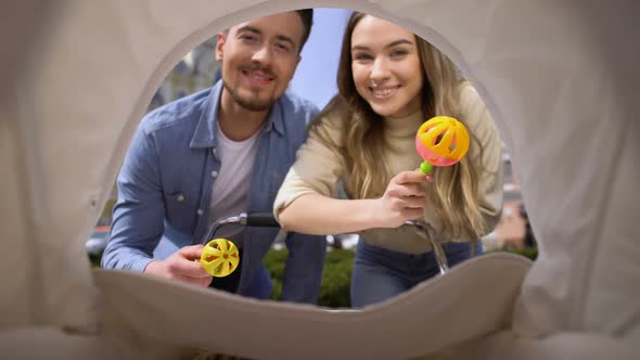 Cheerful Mom and Dad Shaking Rattle Toys Front of Newborn in Pram, Parenthood alt
