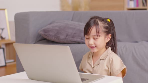 Adorable little girl sitting using computer laptop playing game and social media or chatting with he alt