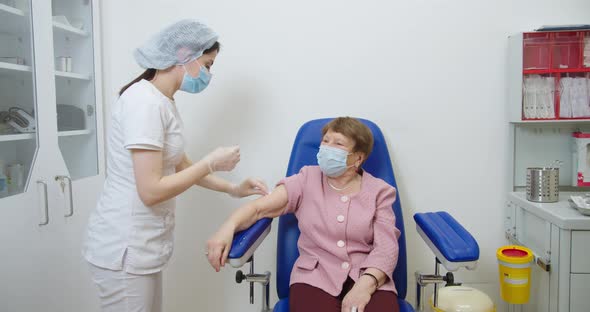 Nurse Wearing Protective Gloves and a Protective Mask Gives a Vaccine Injection To a Old Female