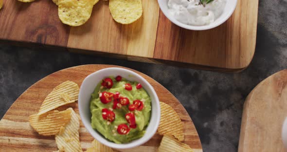 Close up view of variety of chips and sauces on wooden trays on black surface alt