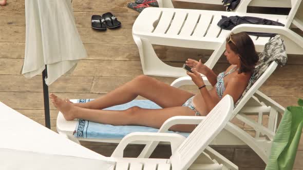 Beautiful Young Women Relaxing on the Deck Chair near the Pool alt