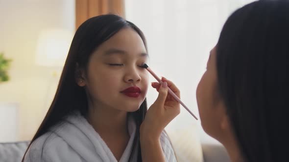 Loving Mother Making Professional Make Up for Her Little Asian Daughter Playing Beauty Salon at Home alt