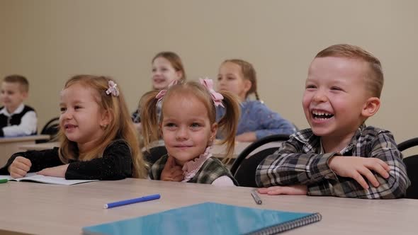 A Group of Children Sit at a Desk in an Elementary School and Laugh alt