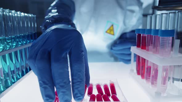 Lab Worker in Protective Uniform Putting Sample Tube with Blood in Container alt