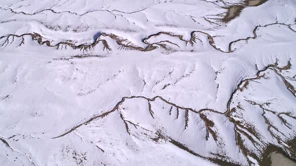 Aerial view flying over cracks in the earths landscape in the snowy desert alt