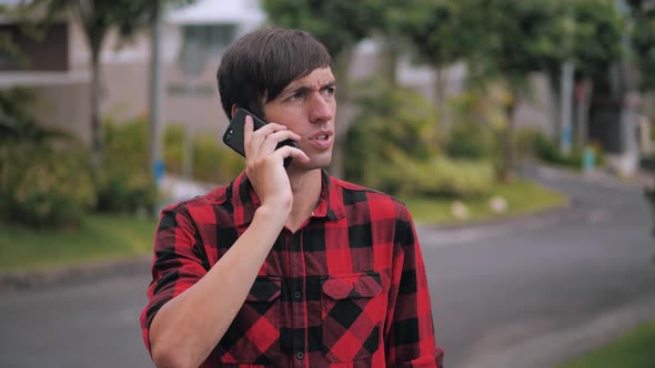 Portrait of Handsome Caucasian Man in Red Plaid Shirt Talking on a Cell Phone at Suburb of the City