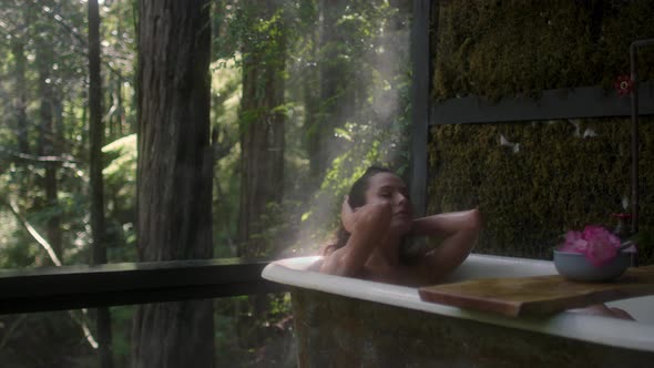 A girl in a bathtub in a forest during the rain. Beautiful young woman relaxing in the bathroom