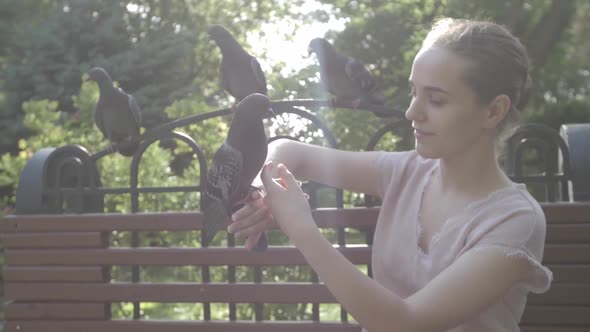 Young Happy Girl Feeding Pigeons in the Park on a Bench