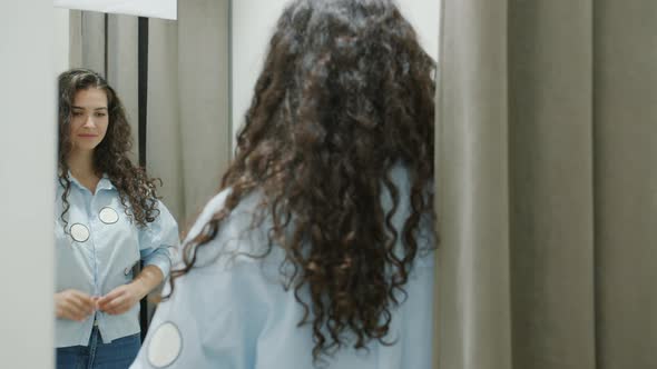 Cute Young Brunette Trying on New Shirt in Changing Room Looking at Mirror Smiling alt