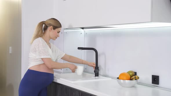 Pregnant Woman Stands Near the Tap Filling Water for Drinking After a Workout a Side View of a Lady