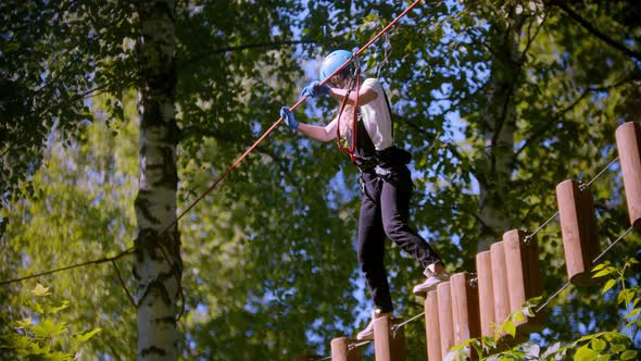 A Woman Carefully Walks on Logs Suspended in the Air Between Trees in the Forest alt