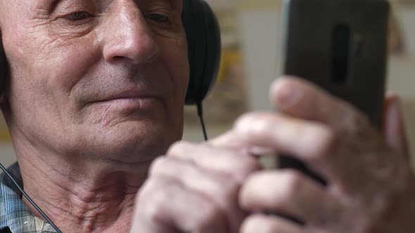Portrait of a cheerful caucasian pensioner over 70 years old in headphones using a smartphone.pressi alt