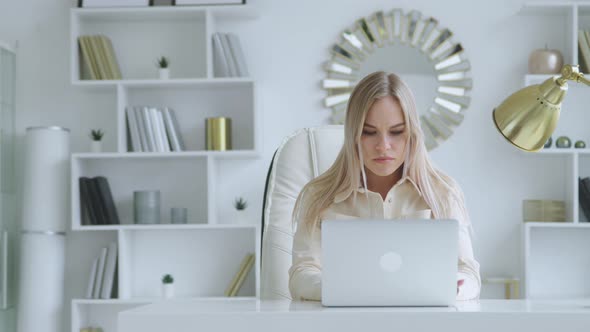 Young female working on a laptop at the desk in a white room. Woman typing on laptop alt