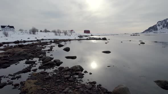 Flying over froozen ocean, rocks and water with the sun reflecting on the surface, revealing a Norwe alt