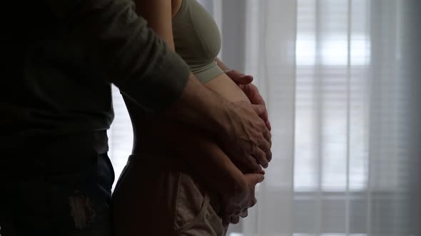 A man walks up to his pregnant wife and strokes her pregnant belly with her alt