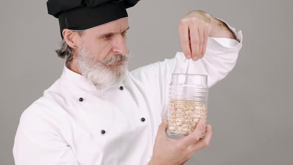Middle Aged Chef Man Pouring Cereals on Grey Background alt