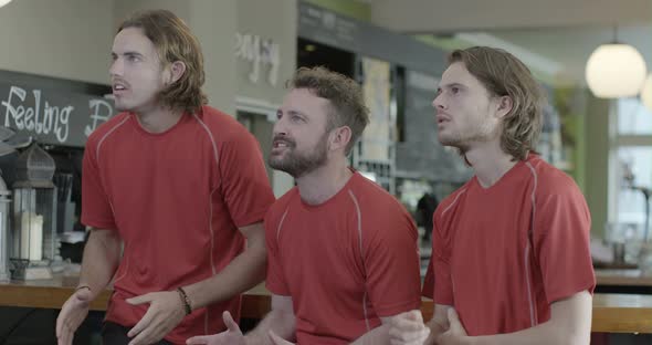 Male friends watching TV and celebrating achievement in pub