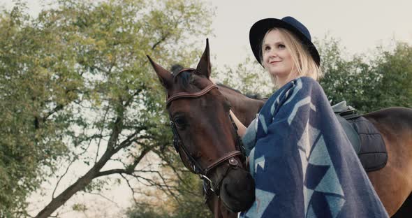 Portrait of a Stylish Woman in a Hat and Poncho Near a Horse alt