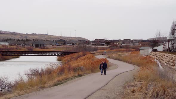 A young couple walking along a river side trail on a blustery overcast windy day in autumn - static alt