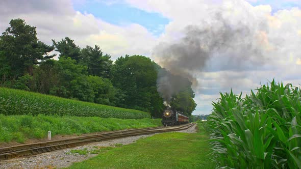 Front View of an Antique  Steam Passenger Train Pulling out of a Stop and Traveling Thru Farmlands a alt