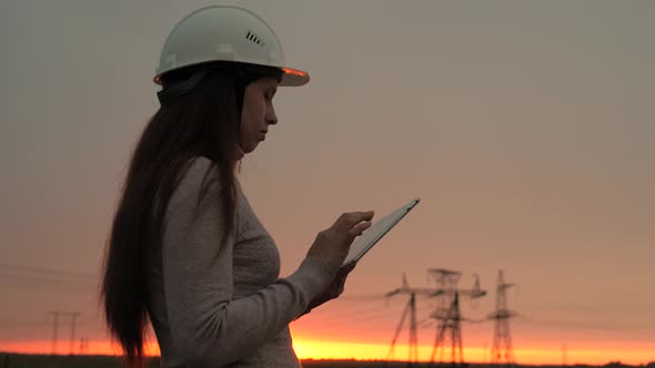 A Woman Power Engineer in White Helmet Inspects Power Line Using Data From Electrical Sensors on a alt