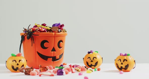 Scary halloween pumpkin printed bucket full of candies against grey background alt