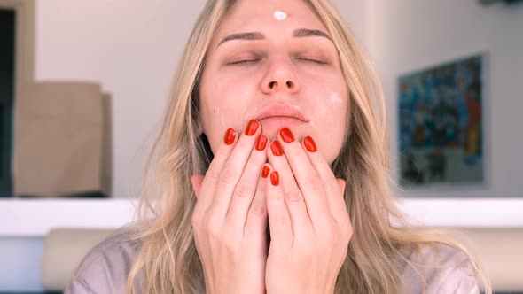 Healthy Young Blueeyed Blonde Woman Applies Nourishing or Flabbing Cream to Her Face
