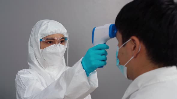doctor in protective PPE suit using infrared thermometer measuring temperature with people