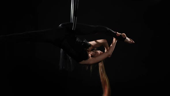 Slim Young Woman in Black Costume Hanging on Air Hoop Spinning Bending at Background alt